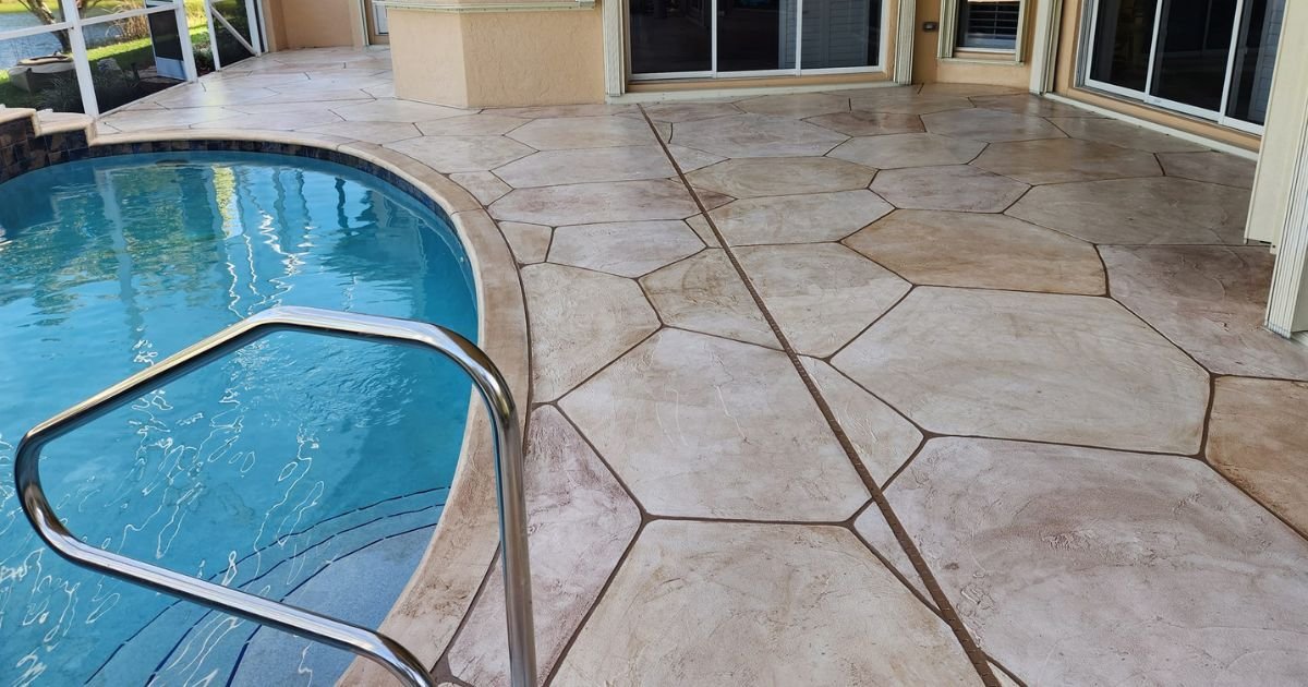 A bespoke colored and textured concrete pool deck by JustFaith showcases a sophisticated design, harmonizing with the luxury outdoor living space while offering a polished and self-leveling surface that reflects the clear blue sky.