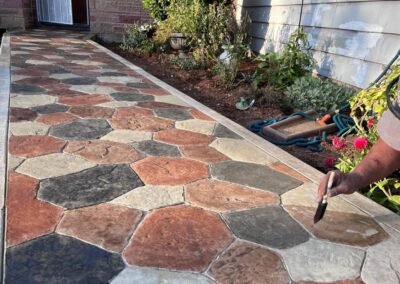 Artisanal decorative concrete pathway with varied stone patterns being finely detailed by a JustFaith Concrete Contractor in Portland, showcasing specialized craftsmanship in a garden setting.