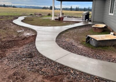 Finished serpentine concrete walkway by JustFaith Concrete Contractors in Portland, surrounded by gravel and green landscape, highlighting meticulous outdoor work.