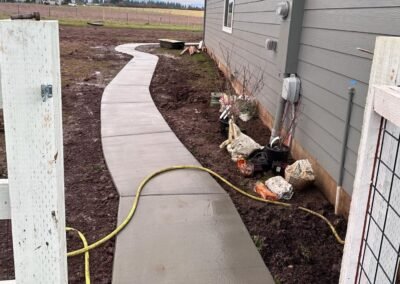 Newly constructed concrete pathway curving alongside a residential building by JustFaith Concrete Contractors in Portland, with tools and materials visible, showcasing work in progress.