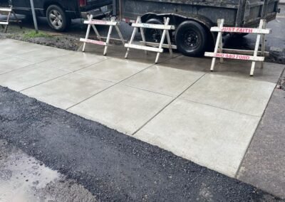 Freshly poured concrete driveway section with saw-cut joints, cordoned off by JustFaith signage in Portland, demonstrating professional concrete contractor work.