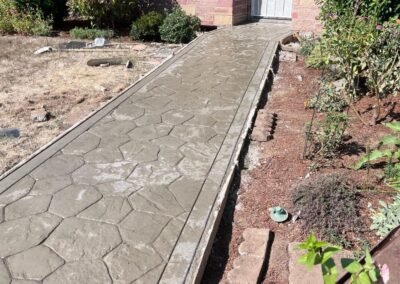 Stamped concrete walkway with a stone pattern finish by JustFaith in Portland, enhancing a residential landscape with construction tools on the side.